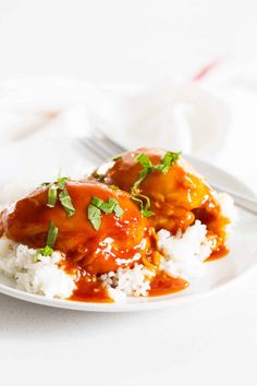 a white plate topped with meat covered in gravy and rice next to a fork