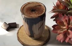 a cup of coffee sitting on top of a wooden coaster next to a flower pot