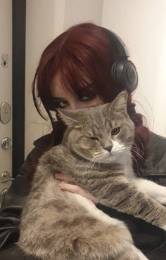 a woman wearing headphones holding a cat in her arms and looking at the camera