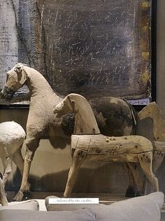 two wooden horses standing next to each other in front of a wall with writing on it