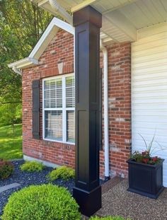 a black clock on the side of a brick building next to a planter filled with flowers