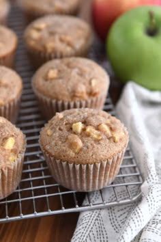 several muffins cooling on a wire rack next to an apple and another green apple