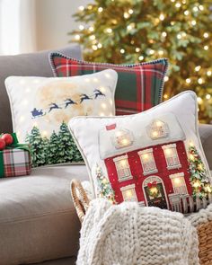 a christmas tree is in the background behind a couch with holiday pillows and blankets on it