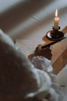 a person writing on a piece of paper with a lit candle in the corner next to it