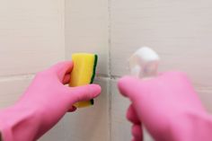 two hands in pink gloves cleaning a wall with a sponge