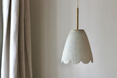 a white pendant light hanging from a wall next to a window with drapes on the windowsill