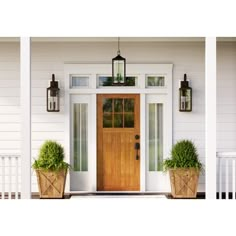 two planters on the front porch of a white house with wood door and windows