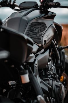 the front end of a black motorcycle parked in a parking lot next to a field