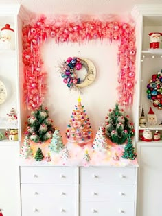 a christmas display in a room with pink and green decorations on the wall, white dressers