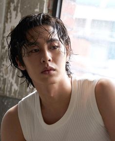 a young man sitting in front of a window wearing a tank top and looking off to the side