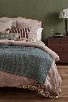 a bedroom with green walls and wooden flooring has a large bed covered in brown linens