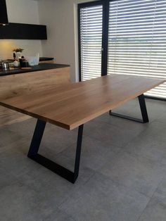 a wooden table sitting in front of a window with blinds on the windowsills