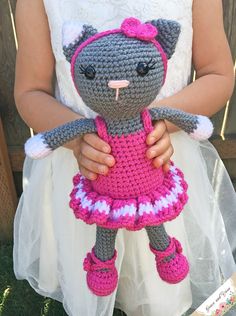 a crocheted cat doll in a pink dress is held by a woman's hands