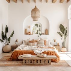 a bed with orange sheets and pillows in a white room next to potted plants