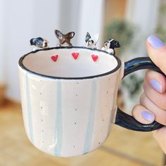 a person holding a coffee mug with tiny birds on it's top and two hearts at the bottom