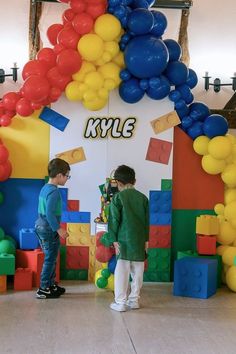 two young boys standing in front of an arch made out of lego blocks and balloons