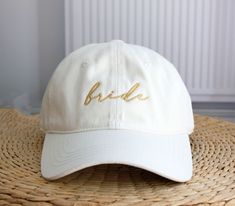 a white hat with the word bride embroidered on it sitting on top of a wicker mat