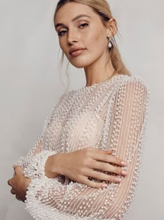 a woman in a white dress with pearls on her shoulders and arms, posing for the camera