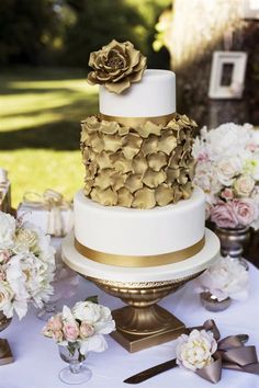 a white and gold wedding cake sitting on top of a table next to other flowers