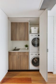 a washer and dryer in a small room with wood flooring, white walls and cabinets