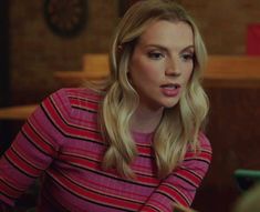 a blonde woman in a pink and black striped shirt is talking to someone on her cell phone