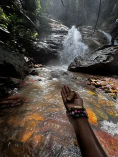 a person's hand reaching out to a waterfall in the jungle with rocks and trees