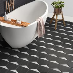 a bath tub sitting on top of a black and white tiled floor next to a potted plant