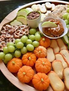 a platter filled with grapes, crackers, apples and other snacks