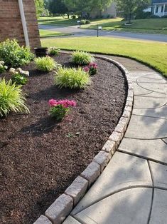 a flower bed in front of a house with flowers growing out of the ground and around it