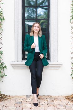 a woman standing in front of a window wearing a green blazer and black pants