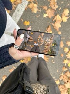 a person taking a photo with their cell phone in front of leaves on the ground