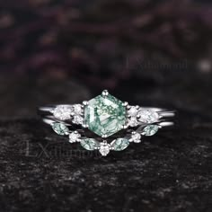 a green and white diamond ring sitting on top of a black stone surface with diamonds around it