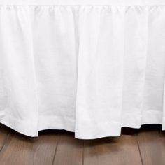 a white bed skirt on top of a wooden floor