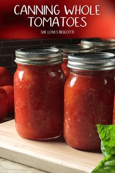 three jars filled with tomato sauce sitting on top of a cutting board next to basil leaves