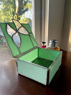 an open green box sitting on top of a wooden table next to a bottle of paint