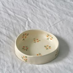 a white bowl with orange and green flowers on it sitting on a white tablecloth