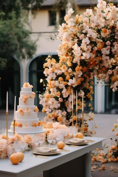 a wedding cake sitting on top of a white table next to flowers and candles in front of a tree