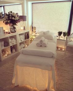 a white bed in a room with lots of windows and candles on the floor next to it