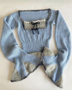 a blue sweater with ruffles and a bow on the front, sitting on a white surface