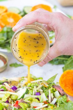 someone pouring dressing into a salad with lettuce, carrots and other vegetables