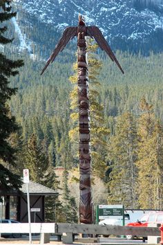 a totem pole in the middle of a parking lot with mountains in the background