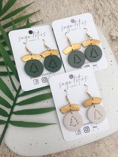 three pairs of earrings with gold and green designs on them, sitting next to a palm leaf