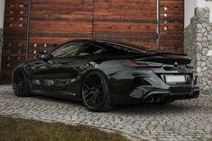 a black sports car parked in front of a wooden garage door and brick driveway area