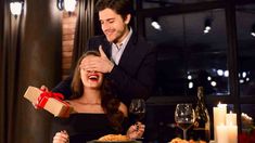 a man giving a gift to a woman at a table with candles and wine glasses