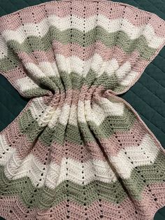 a crocheted blanket is laying on top of a quilted tablecloth with a pink, green and white design