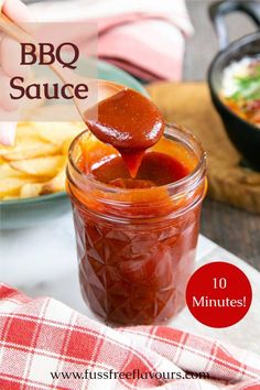 a jar filled with bbq sauce sitting on top of a table next to chips