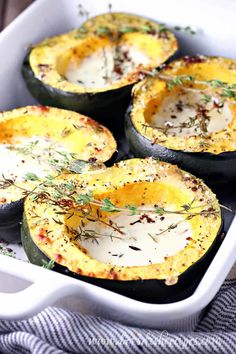 baked acorn squash in a white baking dish with herbs and seasoning on top