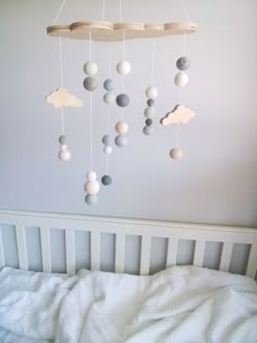 a baby crib with a mobile made out of balls and clouds hanging from the ceiling