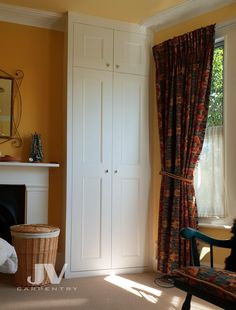 a living room with yellow walls and curtains on the windowsills, a white fireplace and a chair in front of it