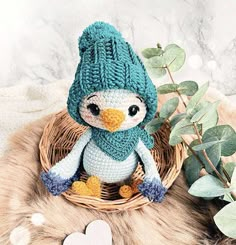 a crocheted penguin sitting in a basket next to a plant